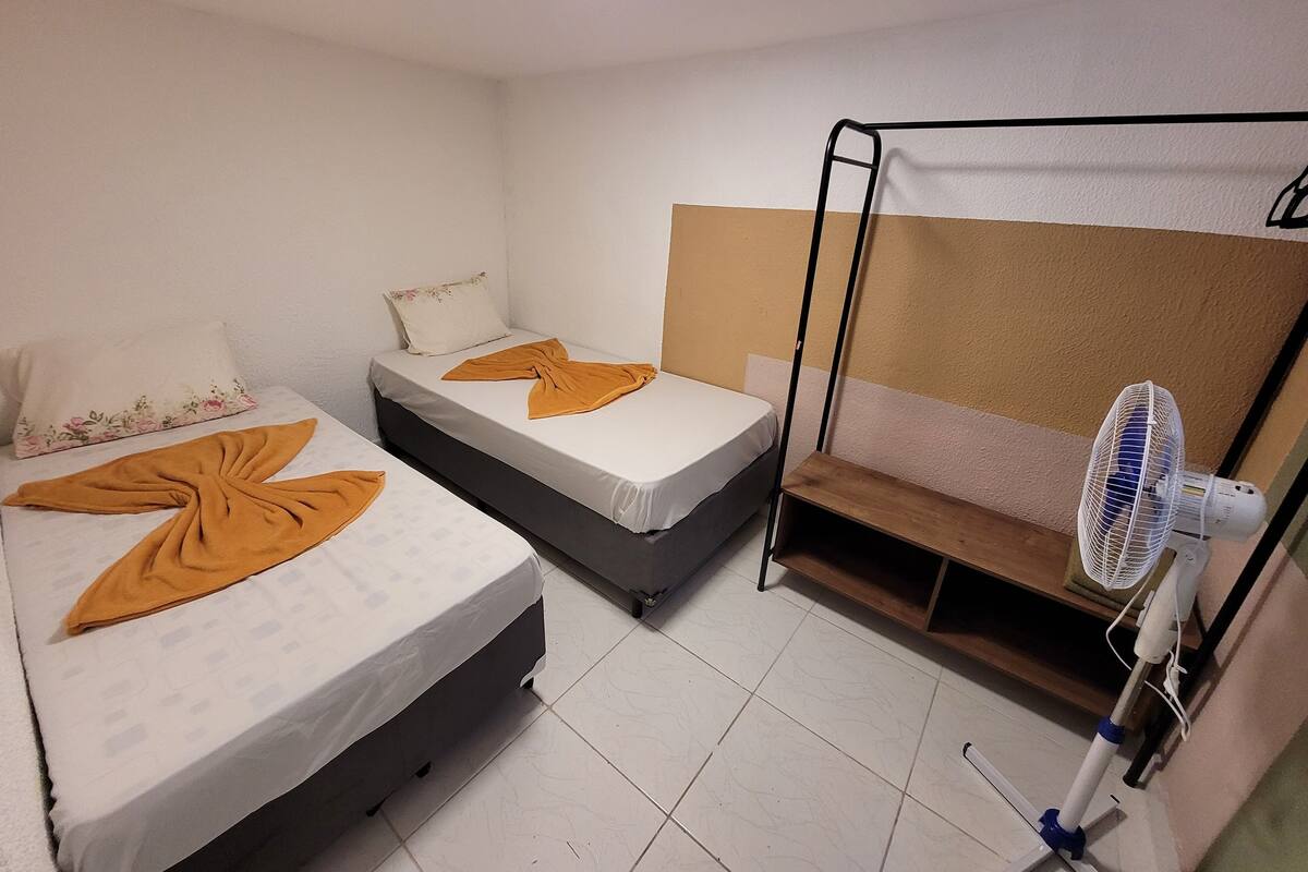Una habitación con dos camas, un ventilador de pie y una repisa de madera.