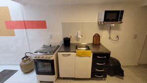 A compact kitchen with a gas stove, oven, sink, and a microwave. - Self Hostel (São Paulo)