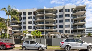 A multi-story hotel with balconies, a covered entrance, and a parking area with cars. - Riverdance Apt 14 (Mooloolaba)