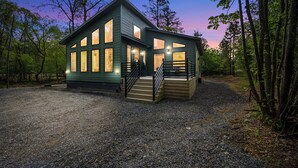 En stuga i två våningar med en grusuppfart och en träveranda.
