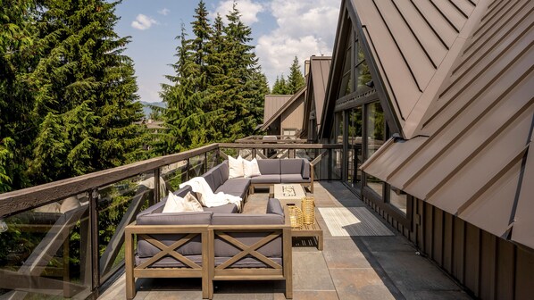 An outdoor seating area with a sofa and a table, surrounded by glass railings and overlooking a forested area. - Ski In/Ski Out | 5BR Luxury Escape | Private Hot Tub | Garage | Managed By Aloha Whistler (Whistler)