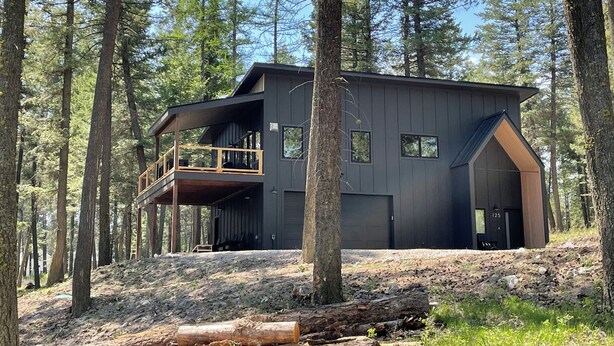 Un chalet moderne à deux étages, doté d’un balcon et entouré d’une forêt.
