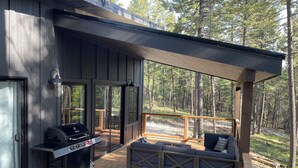 Une terrasse dotée d’un barbecue et d’un espace salon, offrant une vue sur une zone boisée.