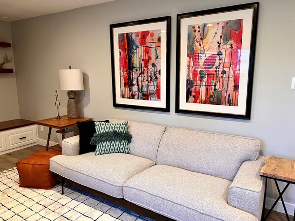 A living room with a grey sofa, a wooden coffee table, and two abstract paintings on the wall.