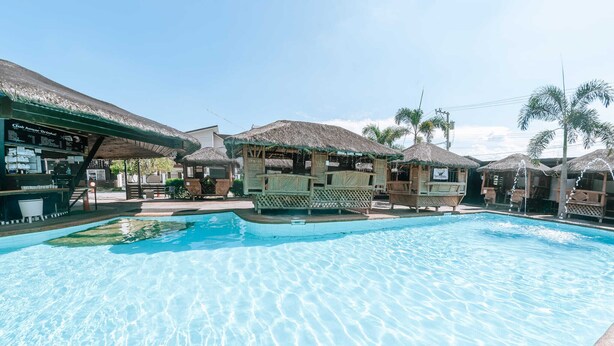 A swimming pool with thatched-roof structures and a bar area.