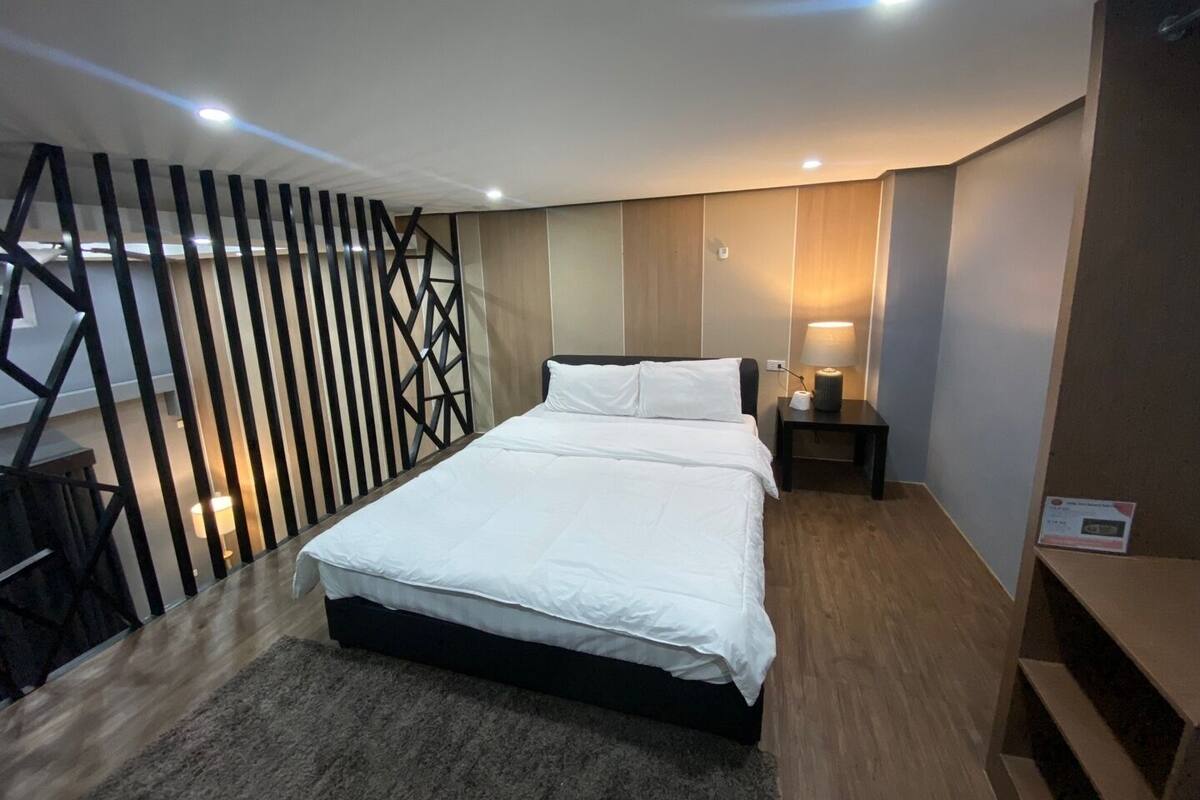 A modern hotel room with a large bed, a nightstand, a lamp, and a decorative wall panel.