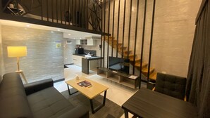 A modern interior with a sofa, a coffee table, and a dining table. There is a kitchen area with a stove and cabinets, and a staircase with wooden steps.