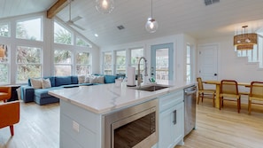 A spacious kitchen with a central island, large windows, and a dining area with wicker chairs.