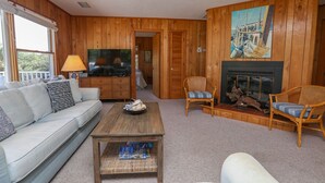 A wooden-paneled living room with a sofa, two wicker chairs, a coffee table, a television, and a fireplace.