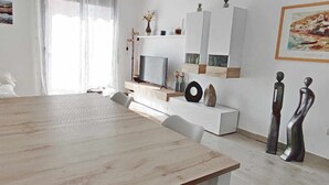Ein modernes Wohnzimmer mit Esstisch aus Holz, weißen Sofas und minimalistischer Einrichtung.