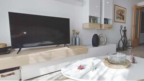 Ein modernes Wohnzimmer mit Flachbildfernseher, rundem Couchtisch und einer Glasbowl, sowie minimalistischer Einrichtung.