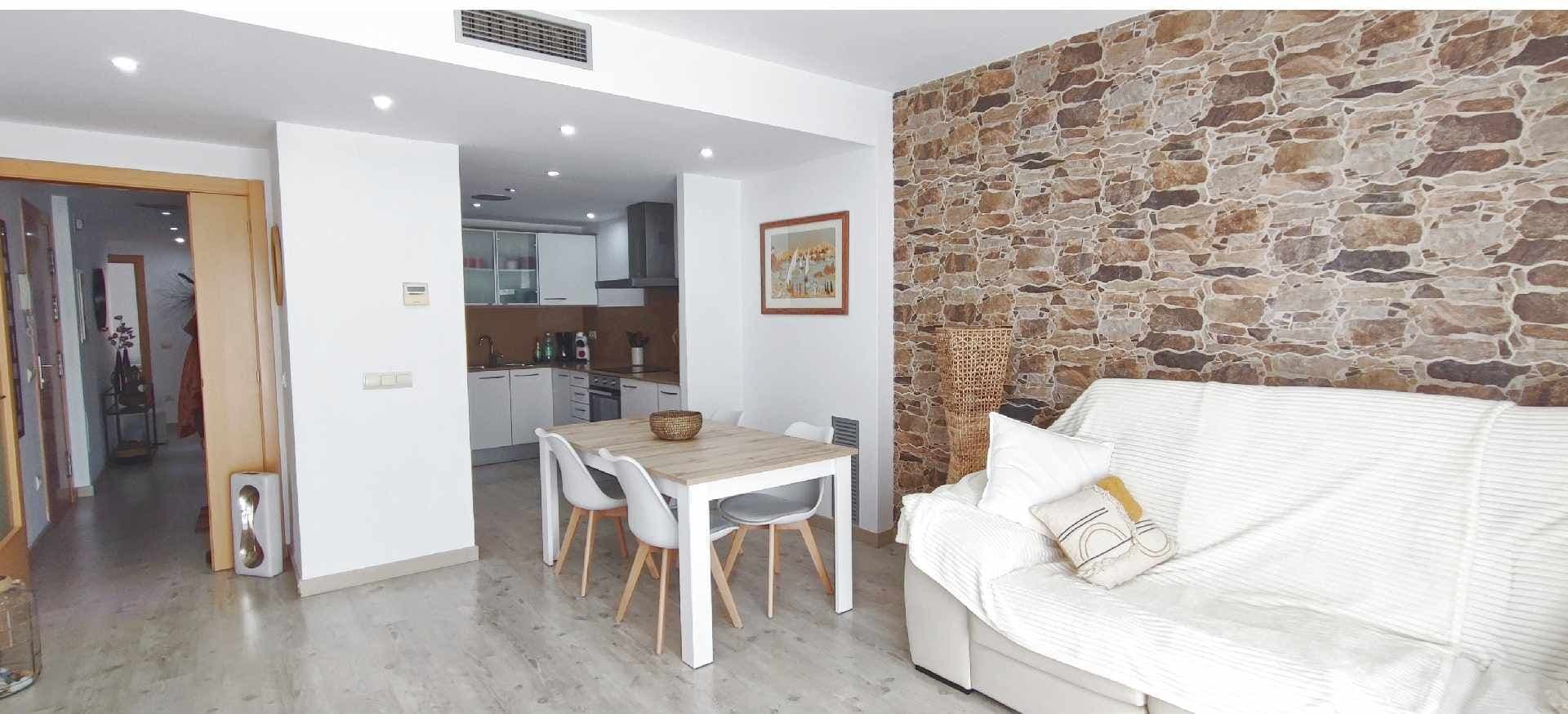 Ein modernes Wohnzimmer mit Steinwand, einem weißen Sofa und einem Essbereich mit Holztisch und Stühlen.