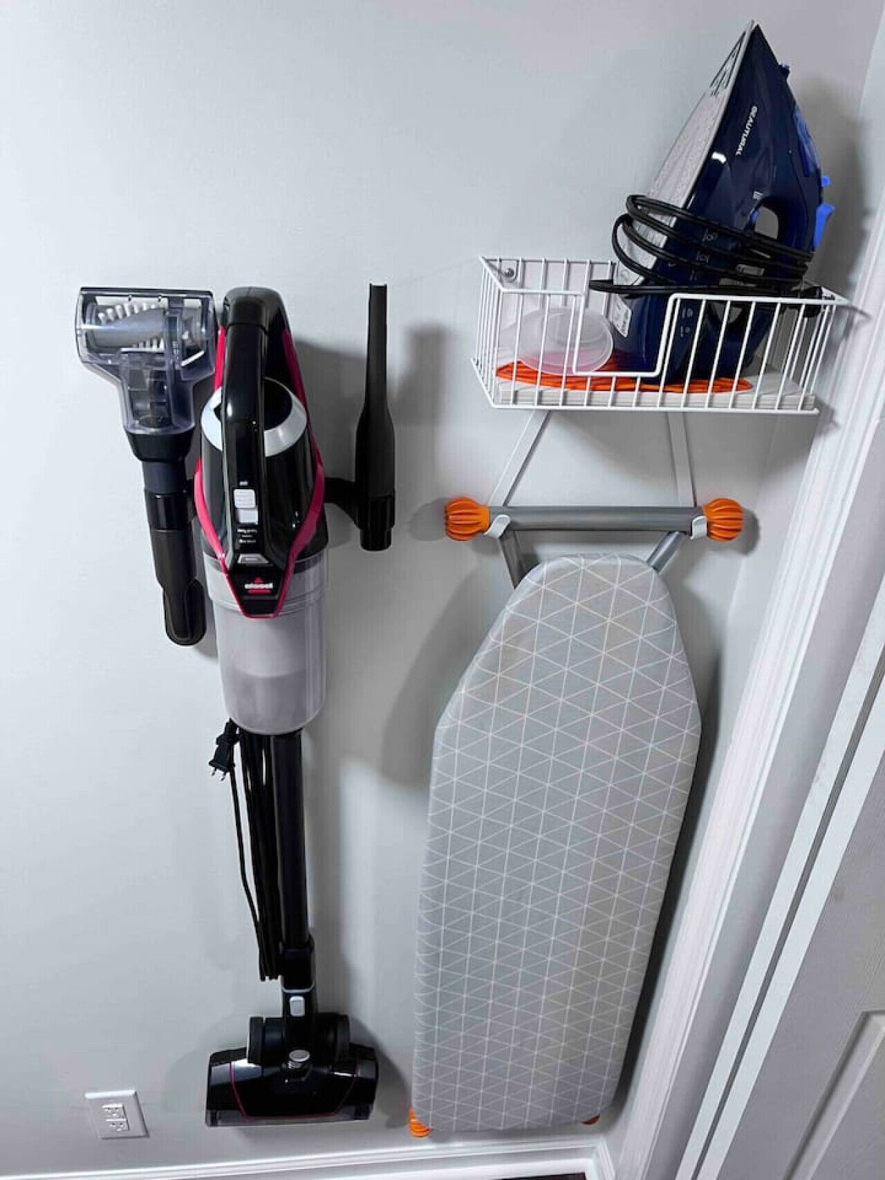 A vacuum cleaner, a wall-mounted shelf with a basket, and a wall-mounted ironing board.