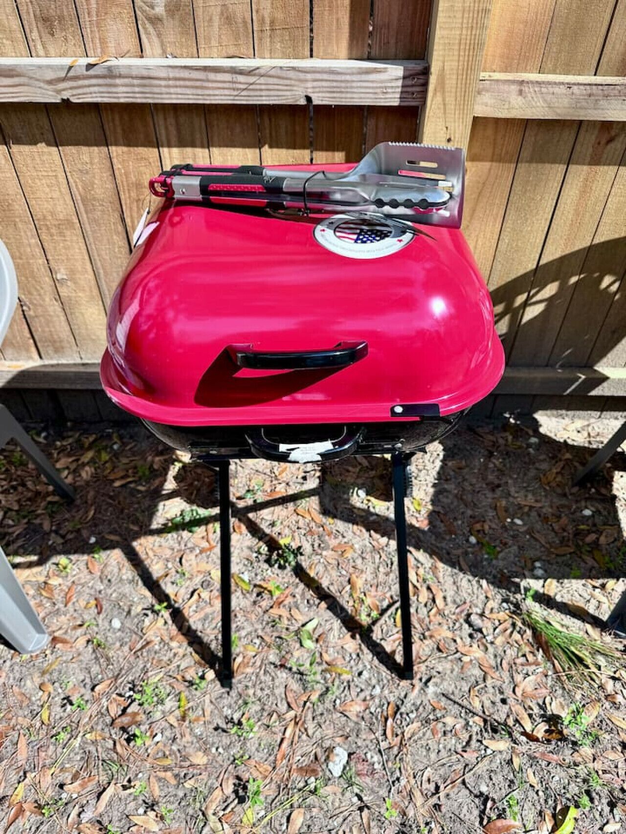 A red barbecue grill on a black stand outdoors.