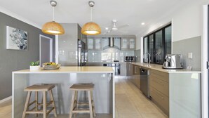 Une cuisine moderne dotée d’un îlot central, de deux tabourets de bar, d’un éclairage suspendu, d’un ventilateur de plafond et d’appareils électroménagers en acier inoxydable.