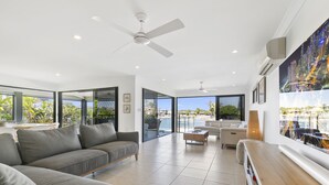 Un salon spacieux avec un canapé gris, une table basse en bois et une vue sur la mer grâce à de grandes fenêtres.