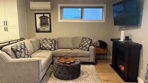 A living room with a sectional sofa, ottoman, fireplace, and a flat-screen TV.