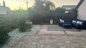 A backyard patio with a stone floor, a dark blue sofa set, and a wooden fence.