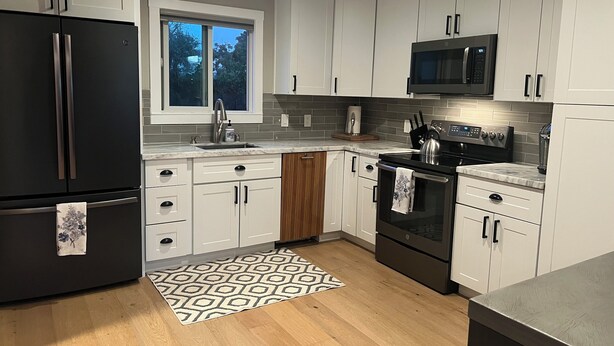 A modern kitchen with white cabinets, a black refrigerator, a microwave, and a stove.