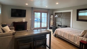 A hotel room with a bed, a desk with two chairs, a TV, a mirror, and a window with curtains.