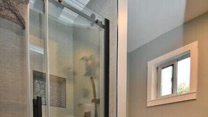 A bathroom with a glass-enclosed shower, a toilet, and a window providing natural light.
