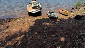 Un barco atracado a la orilla de un lago, con un muelle y una pequeña embarcación en la costa.