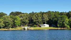 Una propiedad junto al lago con muelle cubierto, una casa blanca y un bosque denso al fondo.