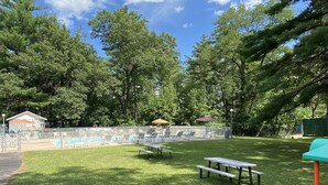 A fenced outdoor area with a pool, lounge chairs, and picnic tables.