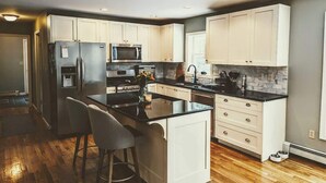 A modern kitchen with white cabinets, a central island, stainless steel appliances, and a black countertop. - Charming Bar Harbor Home w/ Fire Pit & Trails (Bar Harbor)