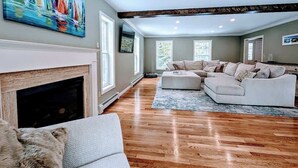A spacious living room with a fireplace, a large sofa set, and a painting of sailboats. - Charming Bar Harbor Home w/ Fire Pit & Trails (Bar Harbor)
