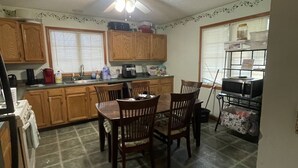 A kitchen with wooden cabinets, a dining table with chairs, a ceiling fan, and a window with blinds. - Come stay at Grandmas house (Springfield)