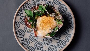 Plat amb un element alimentari en forma de cor, decorat amb vegetació i flors, damunt d'una plat de ceràmica amb dibuixos.