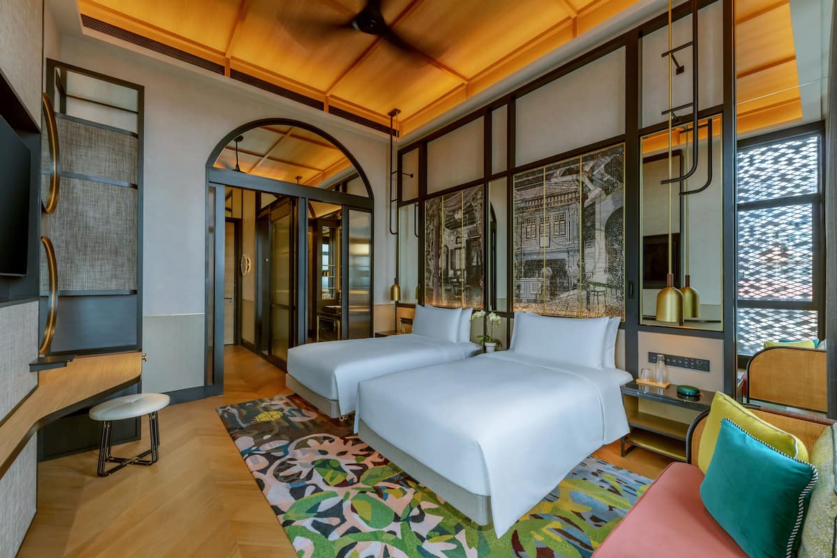 Een moderne hotelkamer met twee bedden, een zithoek en een groot raam met kunstwerk.