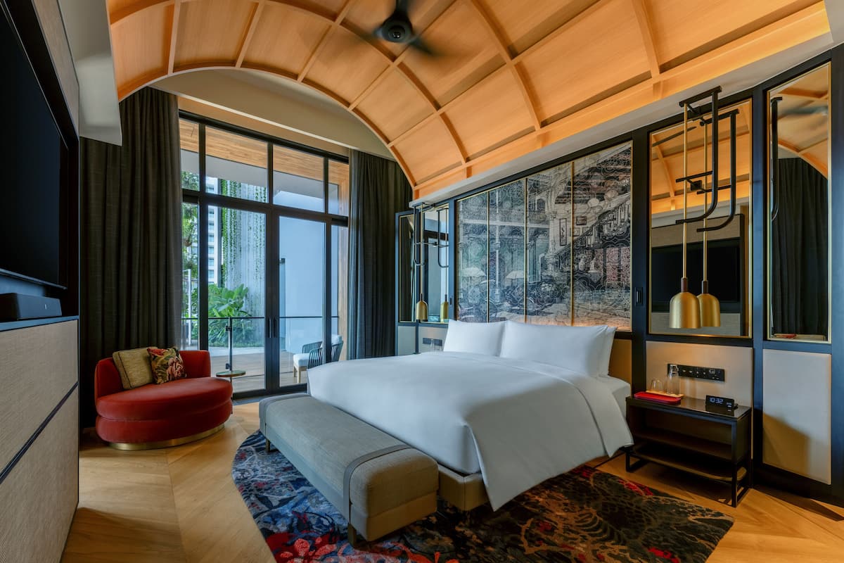 Een moderne hotelkamer met een groot bed, een rode bank, een bankje, een groot raam met uitzicht op de stad en een plafondventilator.