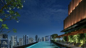 Piscina infinita en la azotea con sillones de descanso y vistas a la ciudad al atardecer.