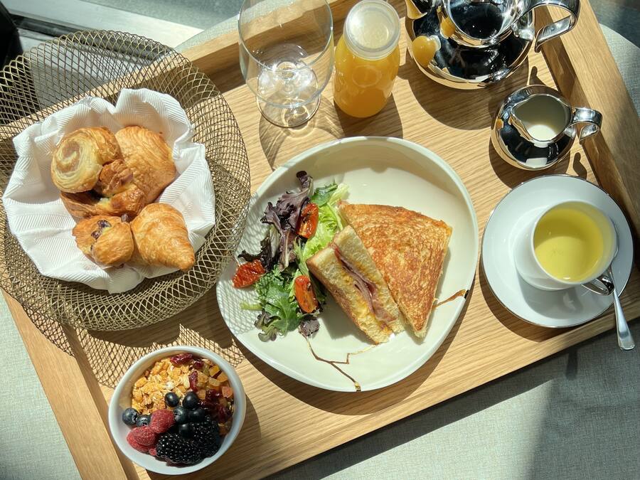 Un vassoio di legno con un panino, un'insalata, croissant e una ciotola di frutti di bosco e granola.