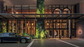 Una entrada de hotel moderna con jardín vertical, puertas de vidrio y un coche estacionado adelante.