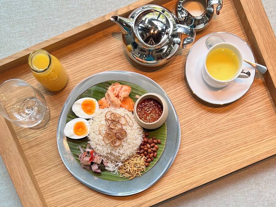 A tray with a plate of food including rice, eggs, peanuts, and fish, a cup of tea, and a glass of juice.