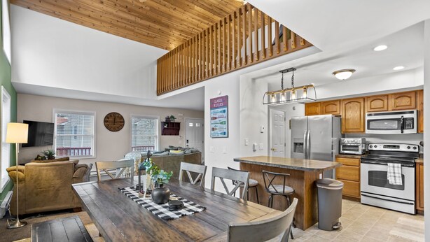 A modern kitchen with wooden cabinets, stainless steel appliances, and a dining area with a wooden table and chairs. - Arrowhead Lake Retreat with large deck and fire pit (Pocono Lake)