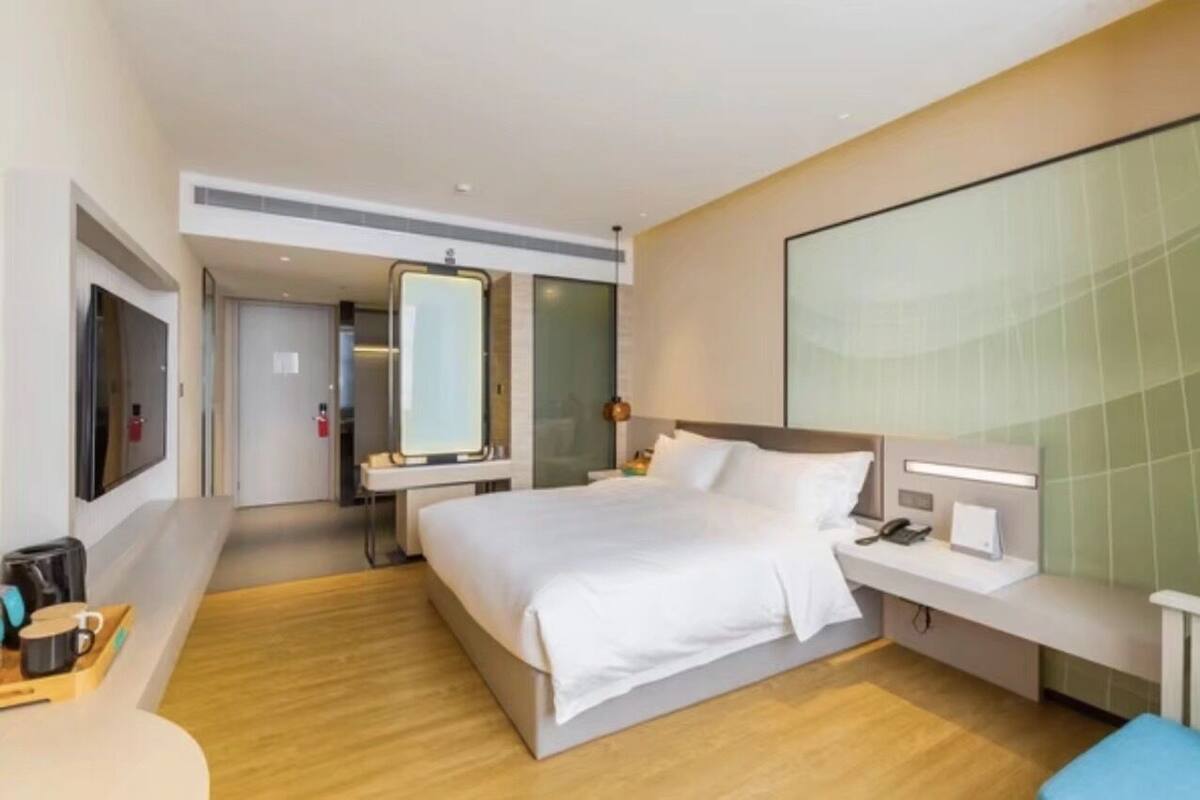 A modern hotel room with a large bed, bedside table, and a large mirror.