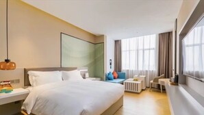Ett modernt hotellrum med en stor säng, sängbord, en liten sittgrupp och ett stort fönster med gardiner.