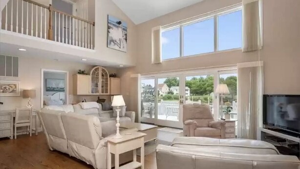 A spacious living room with a high ceiling, large windows, and a balcony.