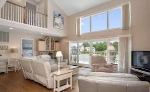 A spacious living room with a high ceiling, large windows, and a balcony. - Waterfront retreat with 4BR, 4.5BA, stunning views & beach 1 mile away!
 (Ocean City)