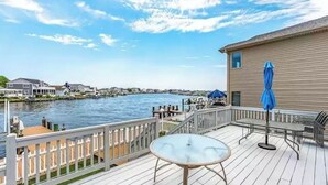 A deck with a table and chairs, overlooking a waterfront with buildings and a dock.