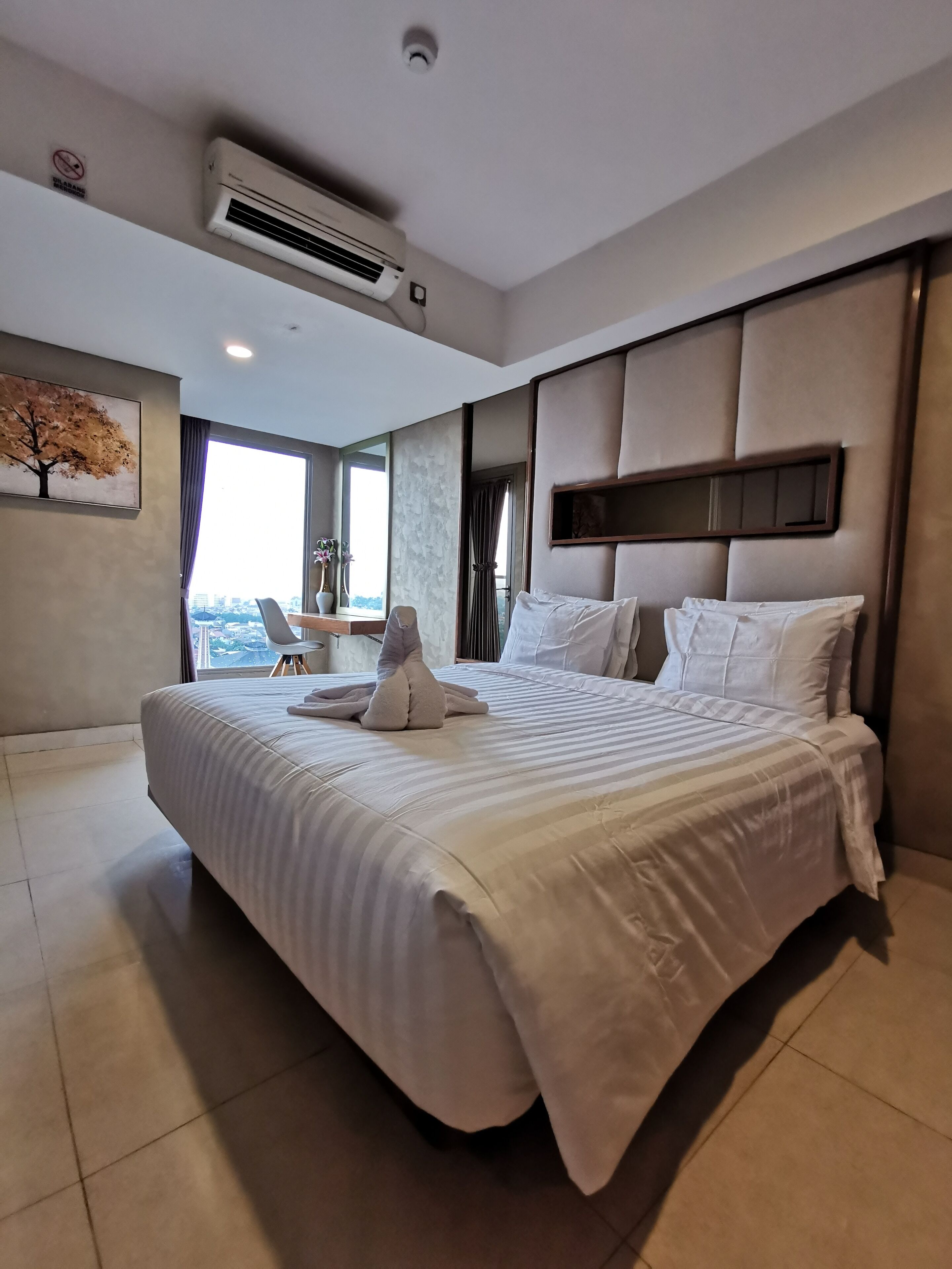 A modern hotel room with a large bed, a view of the city, and an air conditioning unit on the ceiling.