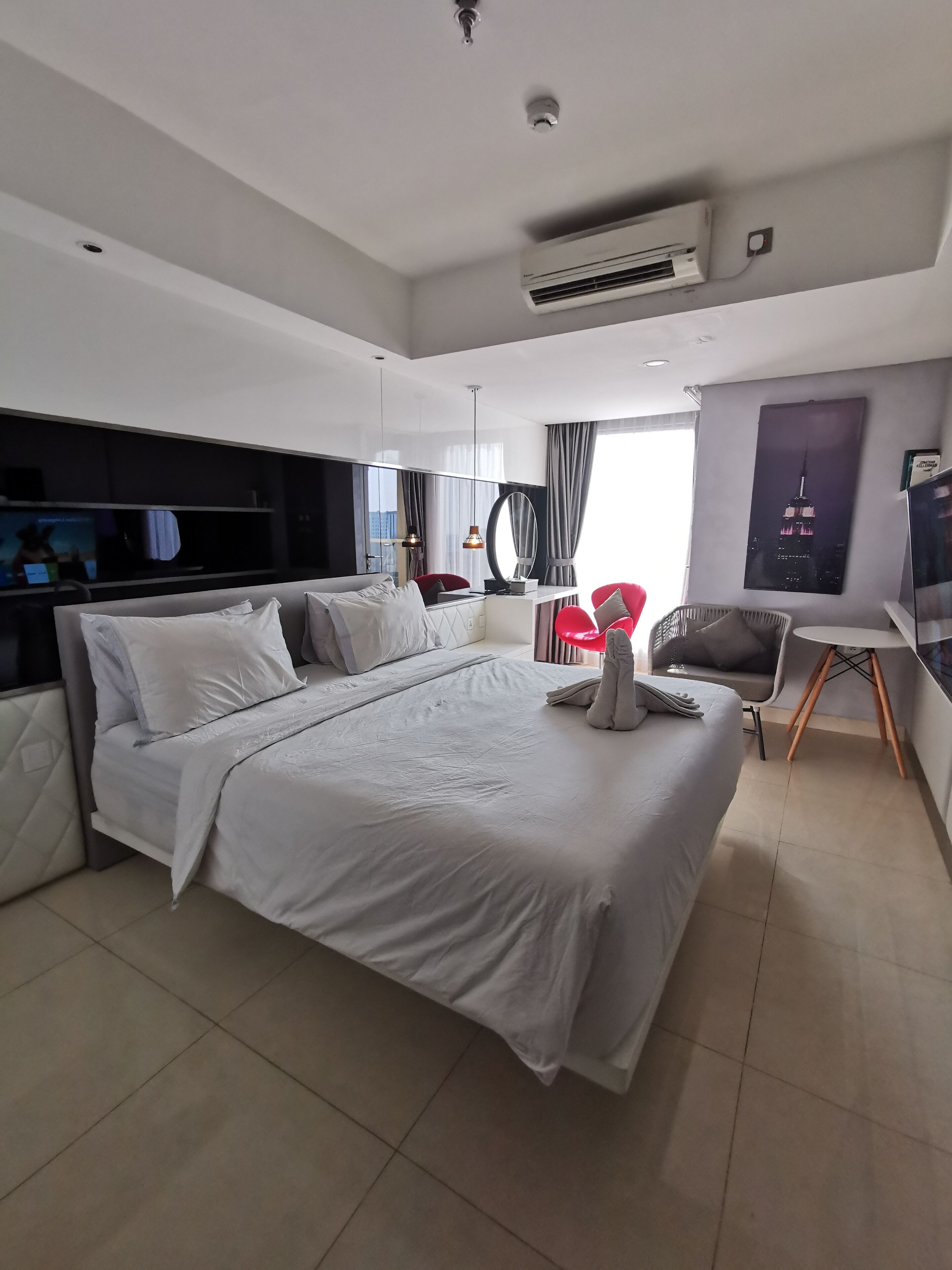 A modern hotel room with a large bed, a desk, a chair, and a TV.