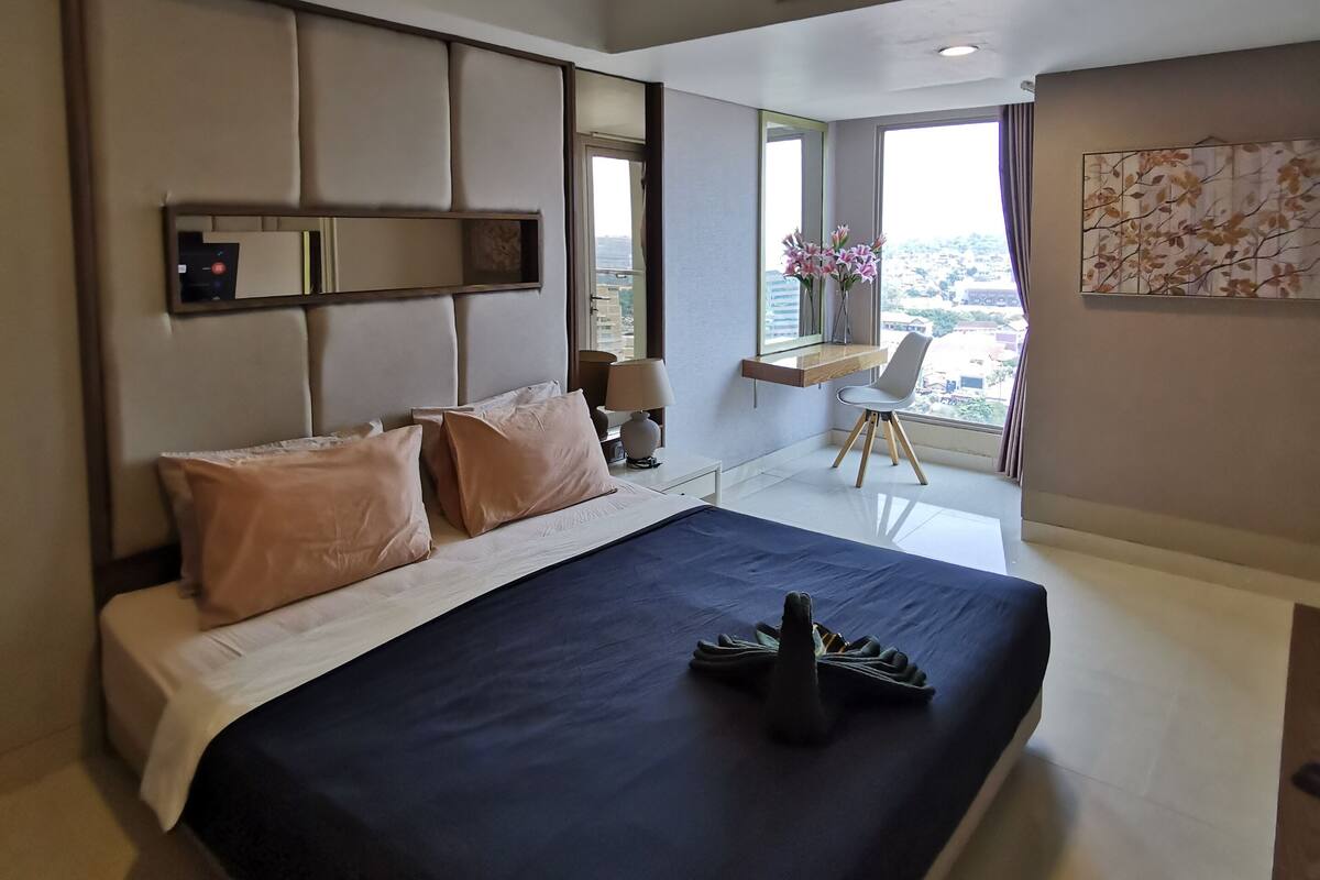 A modern hotel room with a large bed, a desk, and a view of the city.