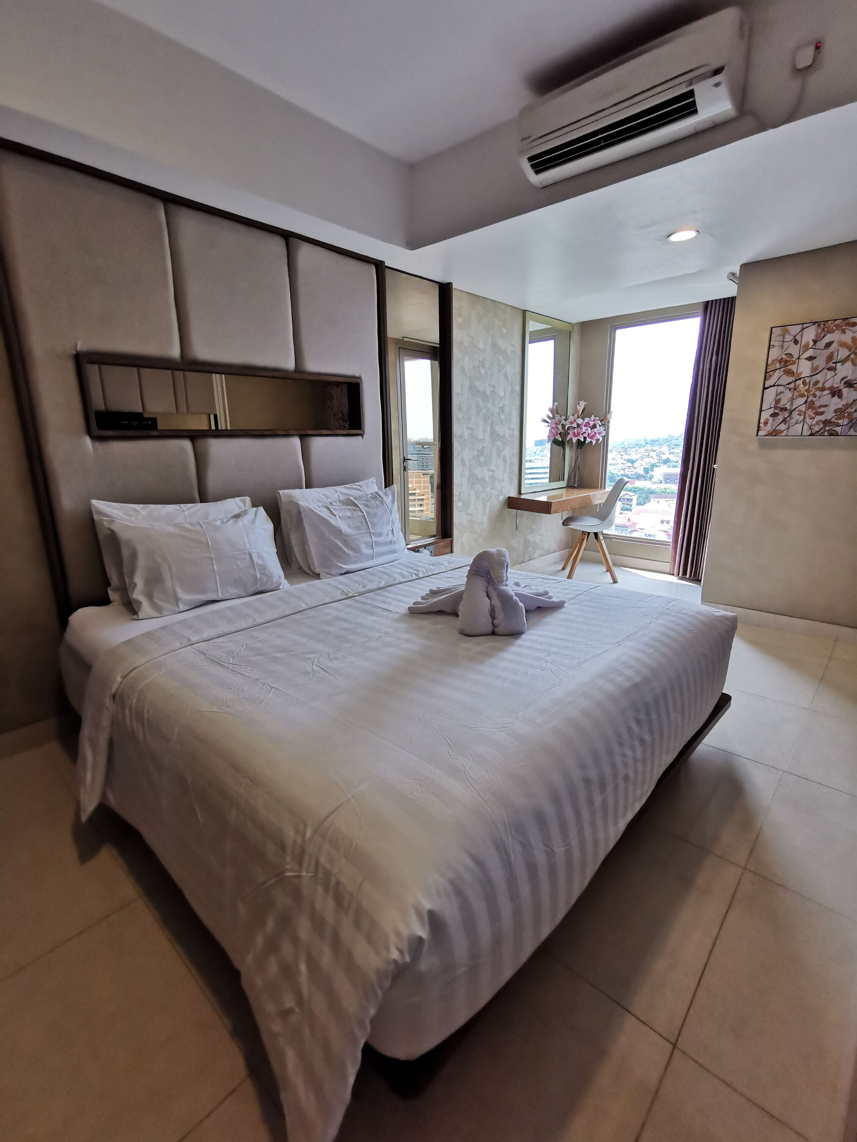 A modern hotel room with a large bed, a desk, and a view of the city.