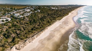 Luftaufnahme einer Küstenlandschaft mit Sandstrand und einer Wohngegend mit Häusern.
