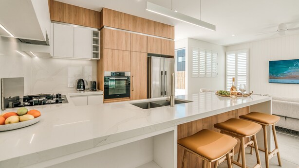 Una cocina moderna con armarios blancos, un refrigerador de acero inoxidable y una encimera de mármol. Hay tres taburetes de madera en la isla.